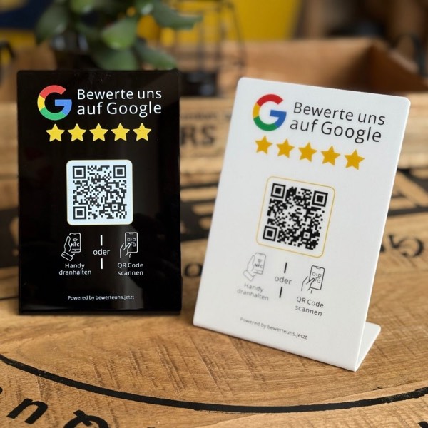 Zwei Bewertungsaufsteller aus Acryl in Schwarz und Weiß mit der Aufschrift Bewerte uns auf Google, fünf Sternen, QR-Code und dem Hinweis Handy dranhalten oder QR-Code scannen.
